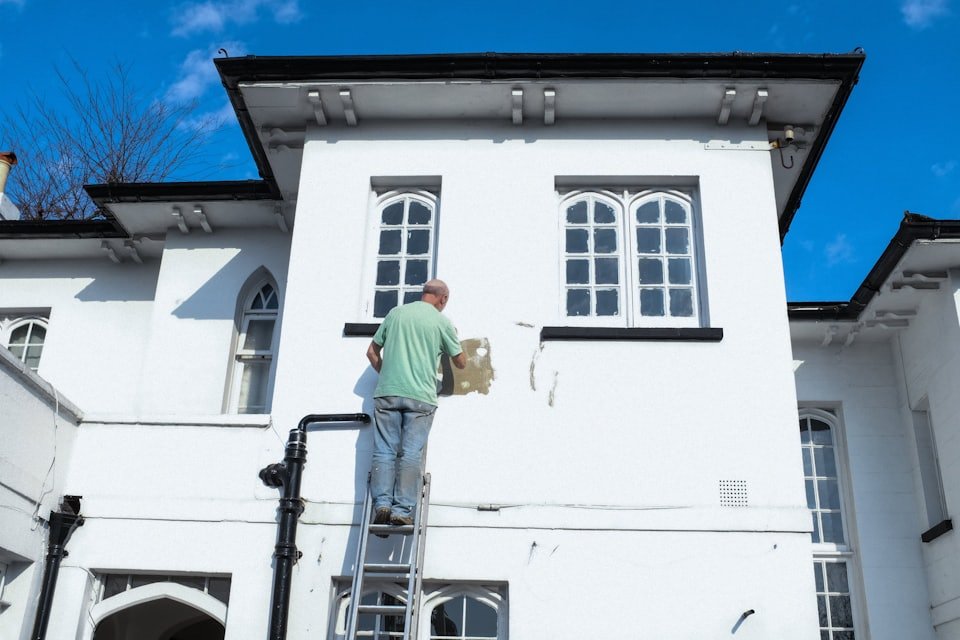 Maler auf einer Leiter bessert den Putz an einer weissen Hausfassade aus